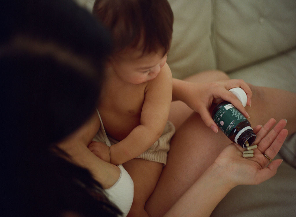 A tender moment of a mother and child as she pours capsules from a bottle of Naternal Vitamins IronBiotic into her hand. The child observes closely, emphasising a shared focus on health and maternal wellness.