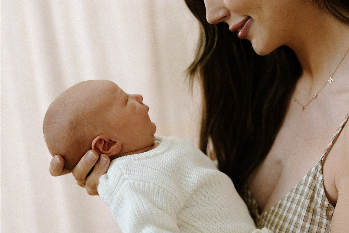 Woman holding a baby wearing a white knitted outfit against a soft pink background