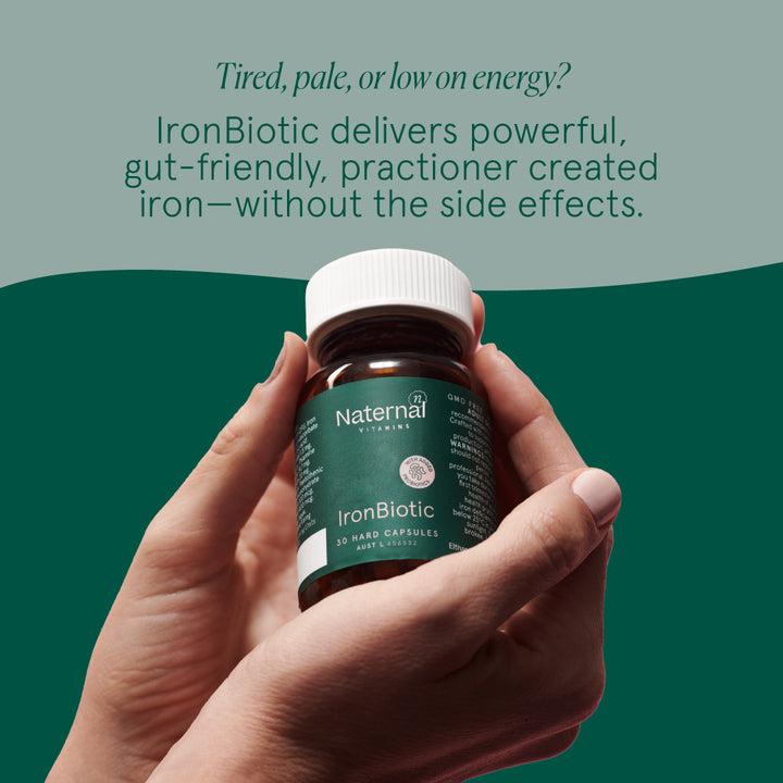 Hand holding a bottle of Naternal IronBiotic supplement with promotional text on a green background