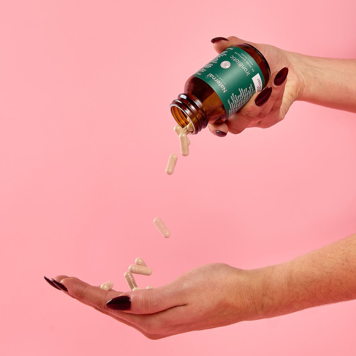 Person pouring pills from a green bottle onto a pink background