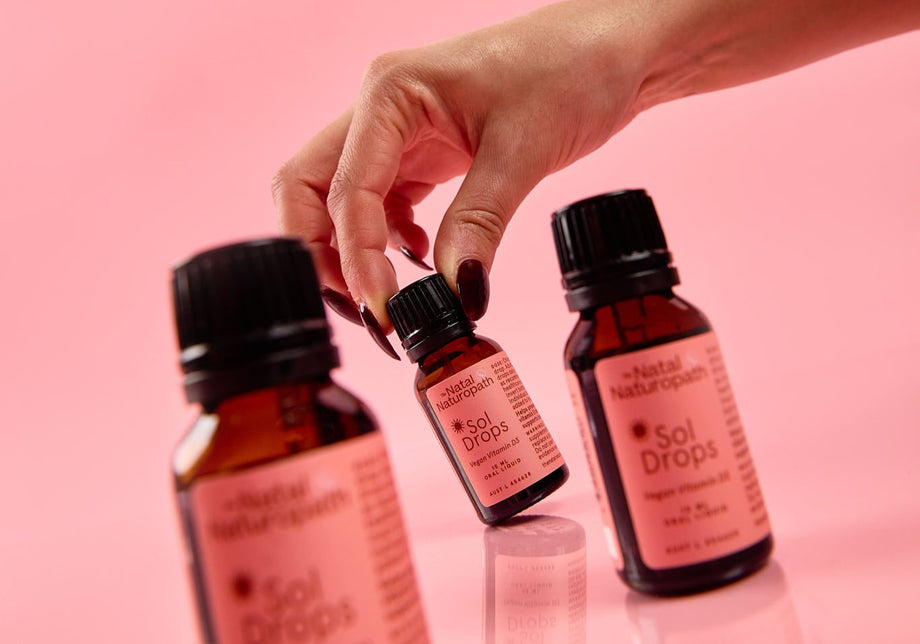 Hand holding three small bottles labeled 'Sol Drops' against a pink background