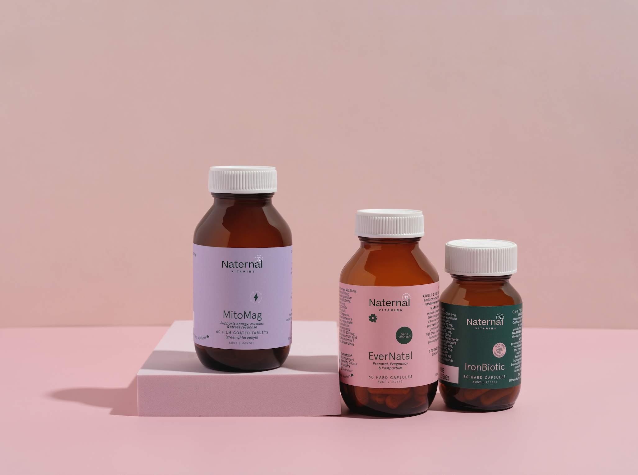 Three bottles of Naternal supplements on a pink platform with a pink background