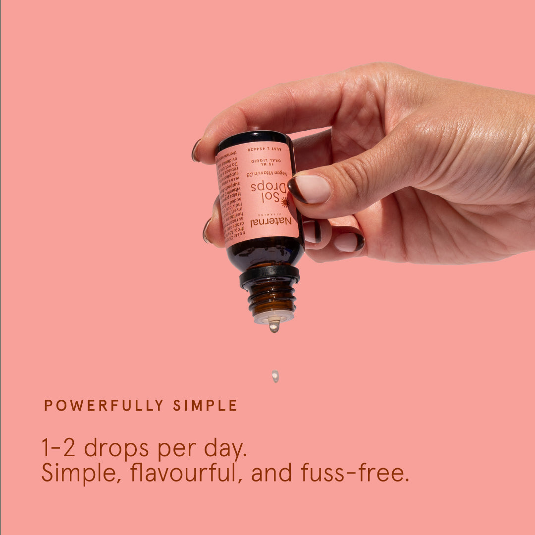 Hand holding a small bottle with a dropper against a pink background