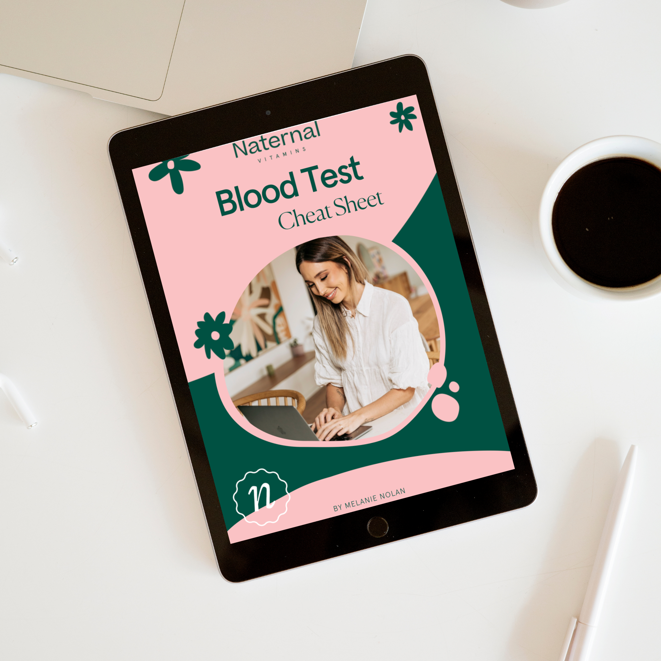 Tablet displaying the Naternal Vitamins 'Blood Test Cheat Sheet' eBook cover, featuring a cheerful woman typing on a laptop. The design uses a pink and green colour scheme with playful floral graphics, creating an inviting and informative digital resource.