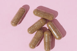 Close-up of Naternal Vitamins' IronBiotic supplement capsules with a granular texture, arranged on a pink background.